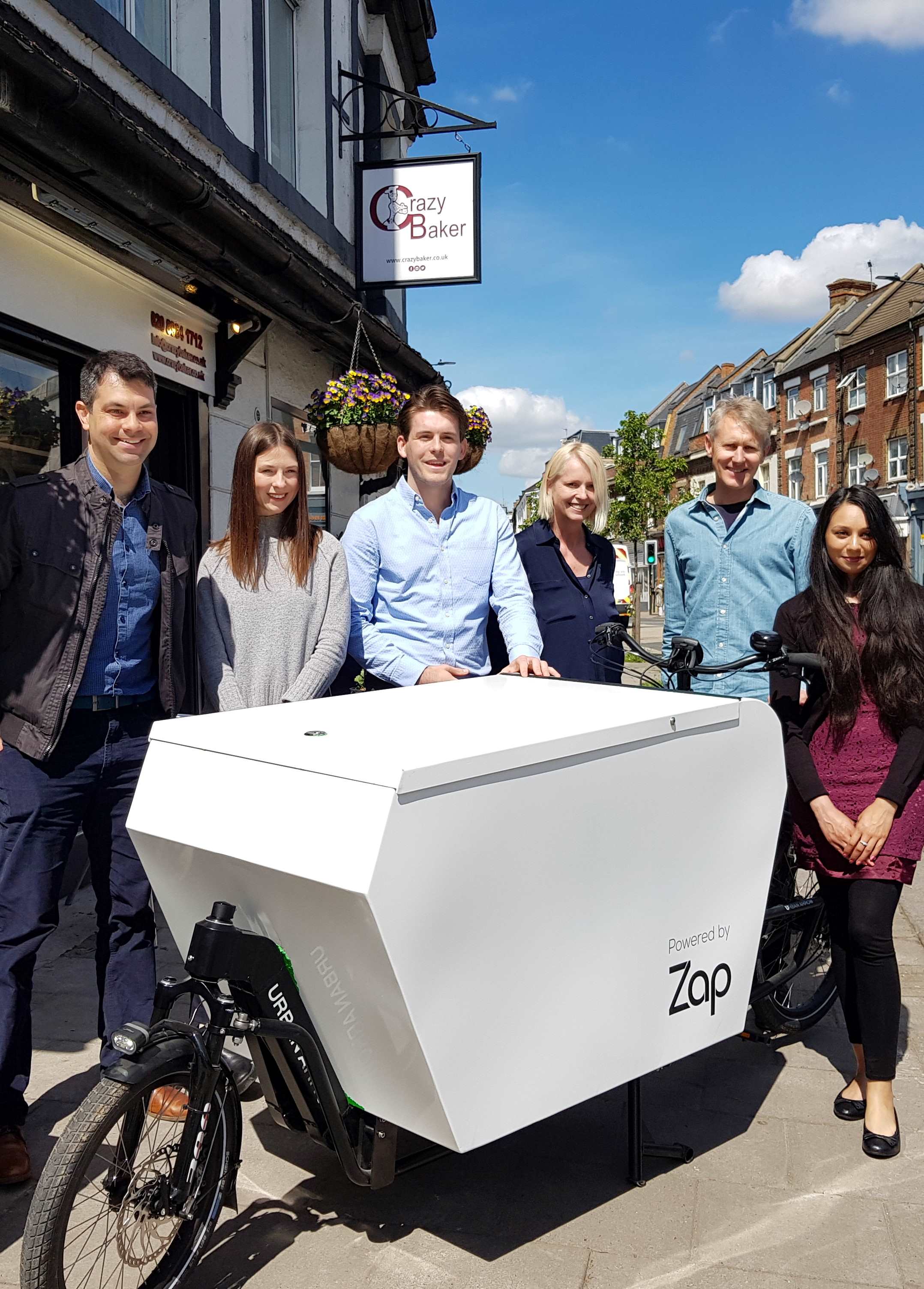 Six people standing around a cargo bike that is outside of a local business