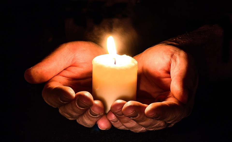 Hands open holding a candle