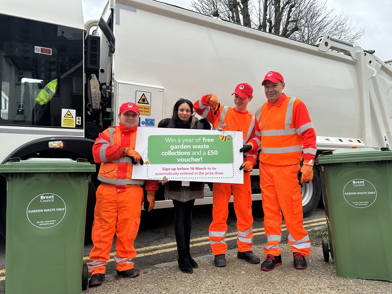 People standing in front of a waste collection lorry, wearing orange uniforms next to binsins