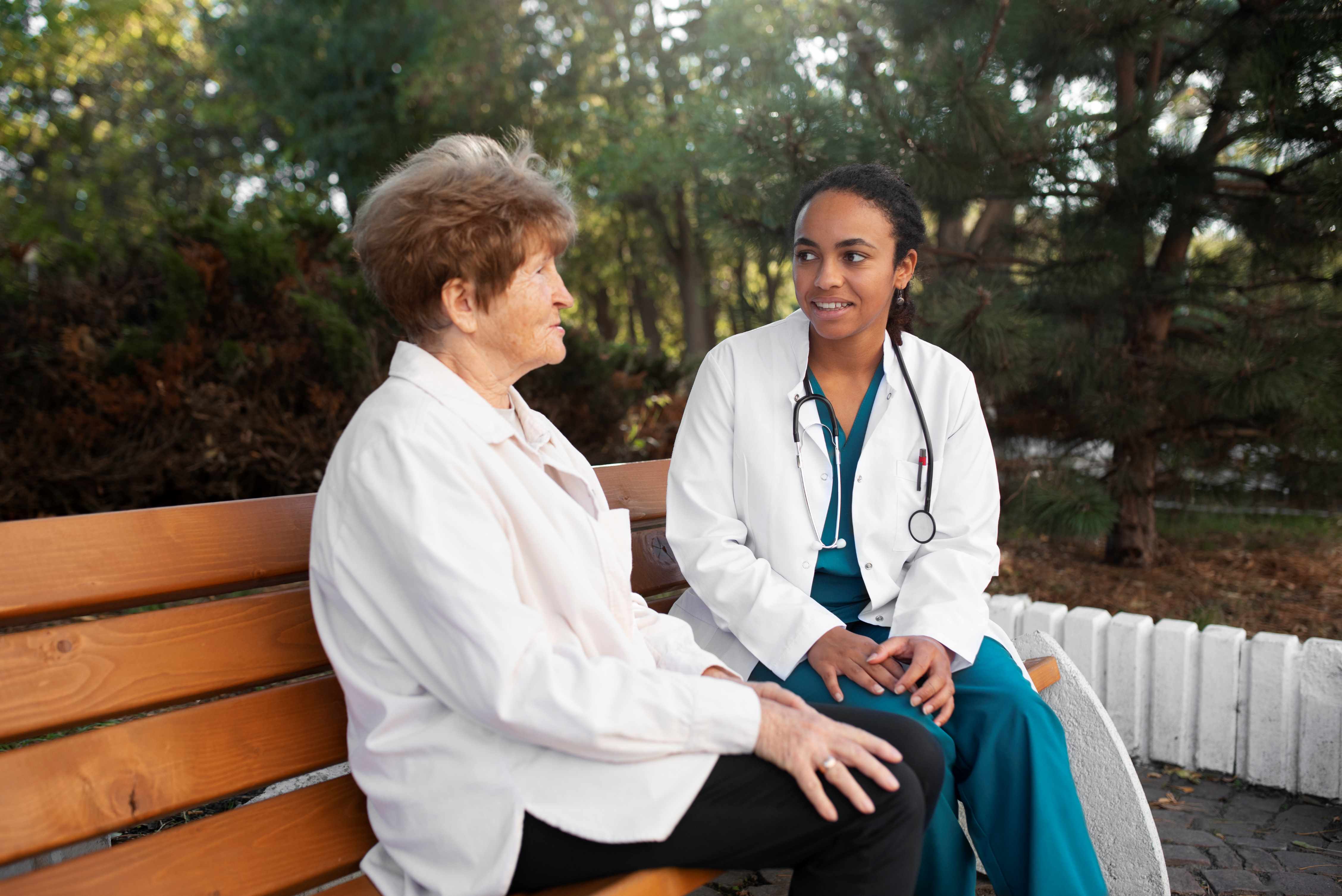 A femaler doctor sitting on a bench with a woman outside in hospital grounds