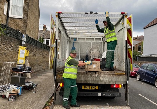 Two refuse collectors standing on the back of a van