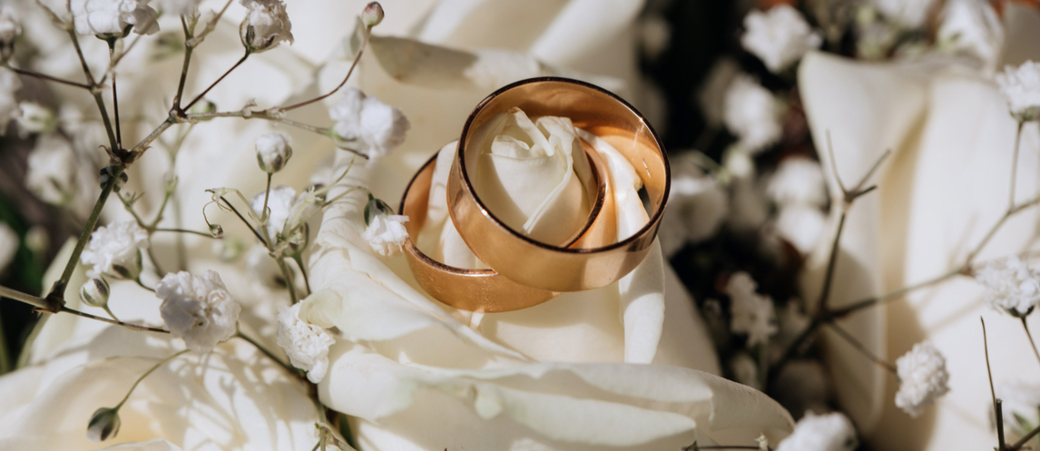 Image of a flower bouquet of white roses and two golden rings on top. 