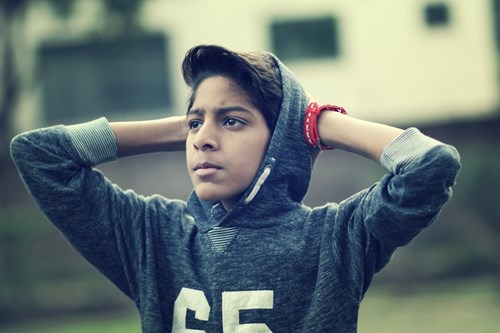 A young boy wearing a hat and a hooded jumper, with his hands back over his ears