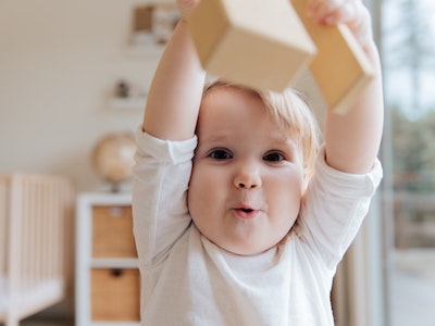 toddler walking to the camera holding a block in the air