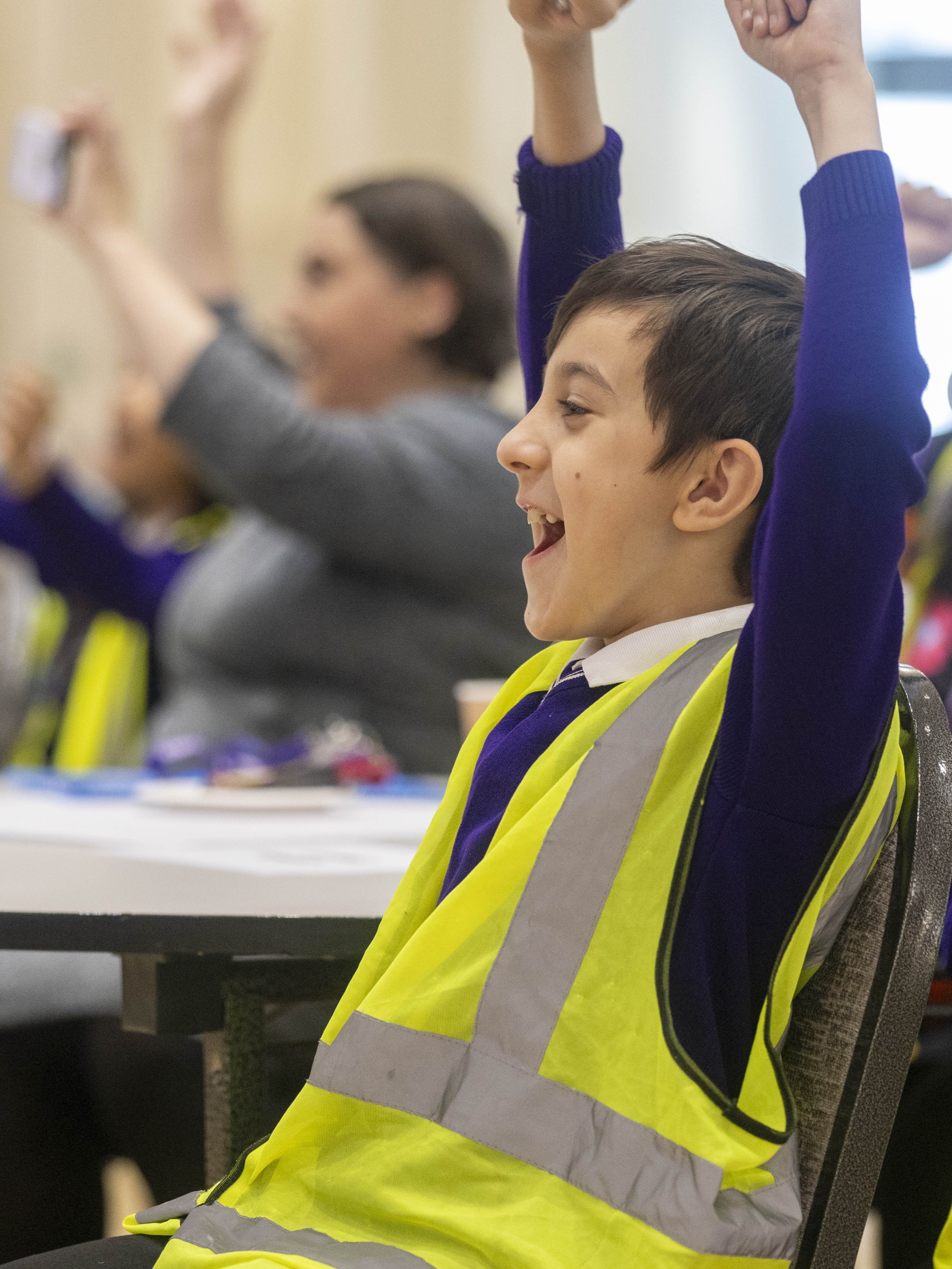 School boy in a high vis jacket with his arms in the air